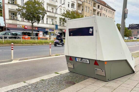 Mobiler Blitzer auf einer Straße mit Blick auf Verkehrszeichen und vorbeifahrende Autos.