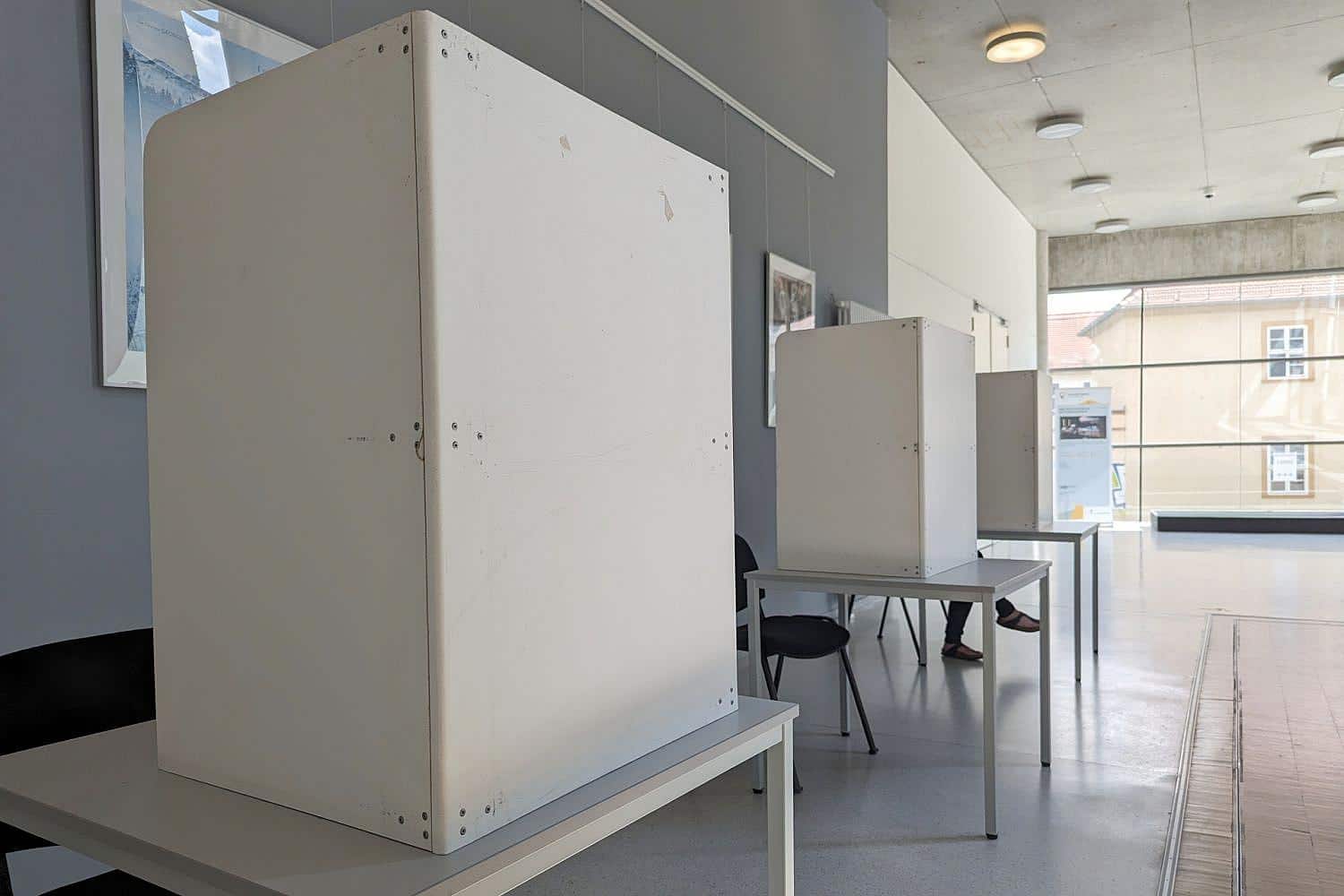 Wahllokal mit Wählern, Wahlurnen und einer Kandidatin im Mittelpunkt der Oberbürgermeisterwahl.