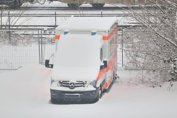 Rettungswagen im Schnee, frostige Temperaturen, stark bewölkter Himmel, neblige Bedingungen, Glättegefahr.