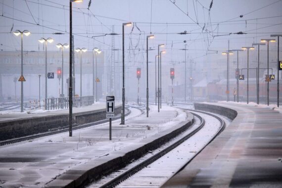 Schneebedeckte Gleise der Deutschen Bahn unter grauem Himmel, frostige Temperaturen und Glättegefahr.