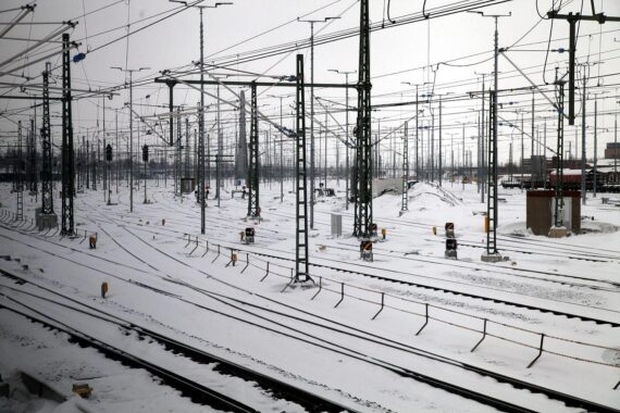 Winterlandschaft mit Schnee, stark bewölkt, Deutsche Bahn im Hintergrund, Glättegefahr.