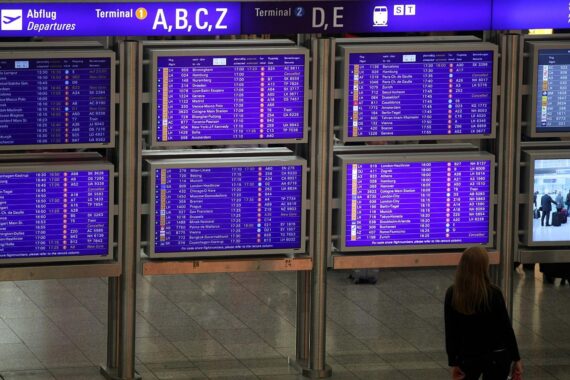 Frau vor Informationstafel am Flughafen zeigt Verspätungen und Streichungen durch Winterwetter.