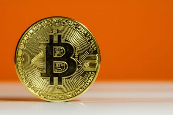 Goldfarbene Bitcoin-Symbolmünze vor orangefarbenem Hintergrund