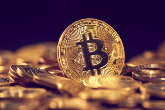 Bitcoin-Symbolmünze zwischen weiteren Münzen vor violettem Hintergrund