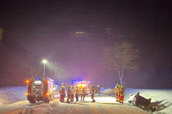 Auto im Straßengraben nach Unfall auf schneeglatter Fahrbahn, Polizei und Rettungskräfte vor Ort.