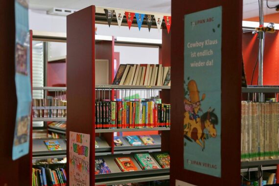 Illustration von Kindern, die in einem Hort spielen, umgeben von bunten Kinderbüchern und Lernmaterialien.