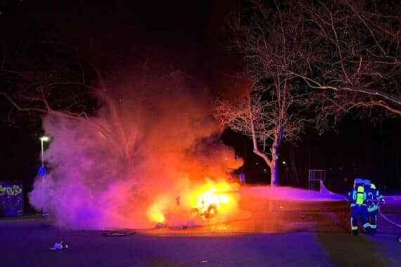 Brennender Tesla auf Parkplatz, Feuerwehr im Einsatz, intensives Feuer und Rauchentwicklung.