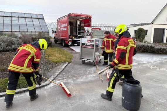 Feuerwehr beseitigt Dieselspur auf Straße, Einsatzkräfte und Gerätewagen bei Arbeit.
