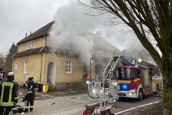 Rauch und Flammen vor einem Reihenhaus, Feuerwehr im Einsatz, tra­gische Brandursache unbekannt.