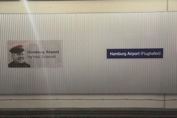 S-Bahnhof Flughafen Hamburg mit Reisenden, Sicherheitskontrollen und Hinweisschildern zum Reiseverlauf.