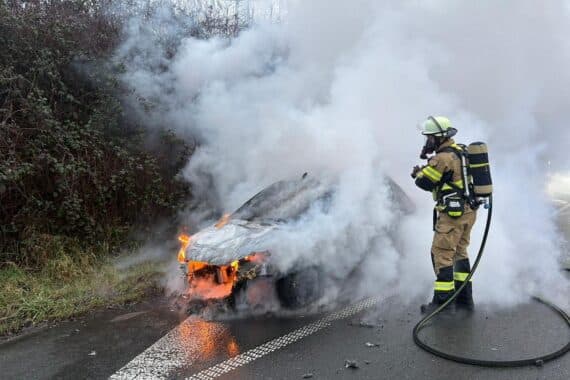 PKW-Brand auf Autobahn, Feuerwehr bekämpft Flammen, starke Rauchentwicklung, Einsatzkräfte sichern die Stelle.