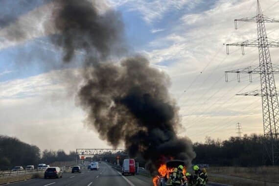 Fahrzeugbrand auf Autobahn, Feuerwehr im Einsatz, Rauch und Flammen aus Motorraum sichtbar.
