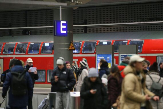 Reisende am Bahnhof warten auf einen Regionalzug, während Sicherheitsdiskussionen über Ticketpersonaliserung stattfinden.