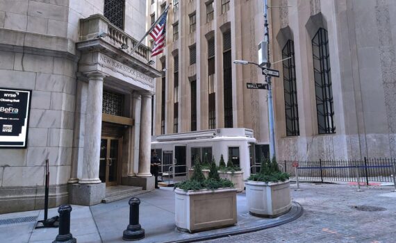 Grafik der New Yorker Börse mit aufsteigenden Kursen und US-Flagge im Hintergrund.