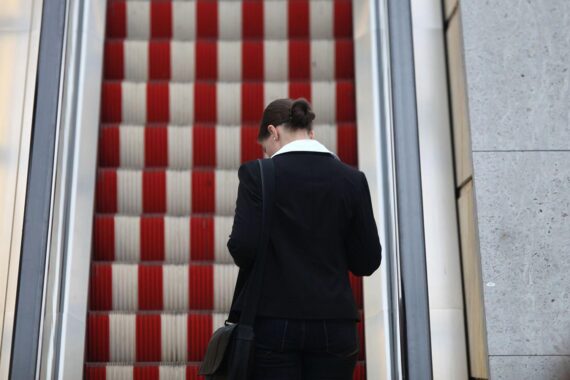 Frau auf Rolltreppe, symbolisiert berufliche Herausforderungen und Gender-Ungleichheit im Arbeitsmarkt.