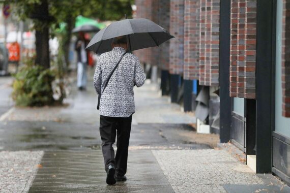 Mann mit Regenschirm unter grauem Himmel, Regen und wechselhaftem Wetter in Hessen.