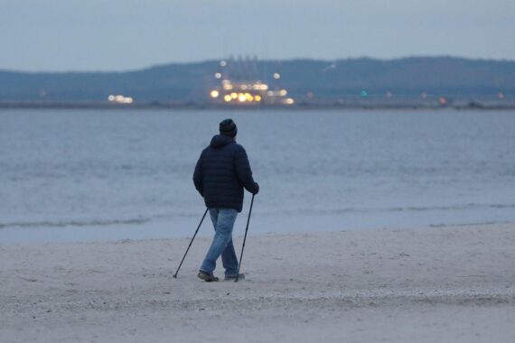 Spaziergänger am Strand unter bewölkten Himmel, Nebelbank zieht vom Wasser ins Landesinnere.