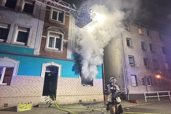 Feuerwehr im Einsatz bei Wohnungsbrand, Rettung von 14 Personen, Flammen schlagen aus Fenster.
