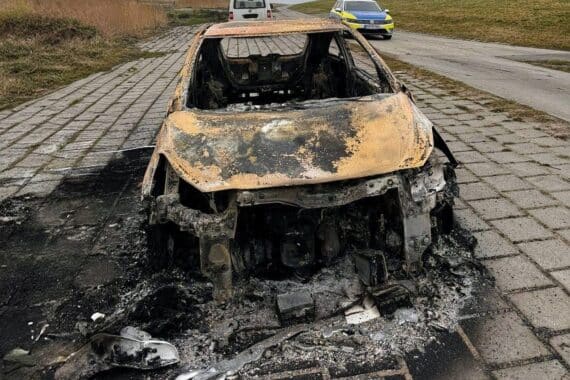 Ein ausgebranntes Opel Corsa-Wrack am Deich, umgeben von Spuren und Ermittlungszeichen.