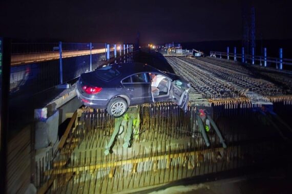 Unfallfahrzeug auf Rohbau-Brücke mit Bewehrungsstahl, umgeben von Baustellenabsperrungen.