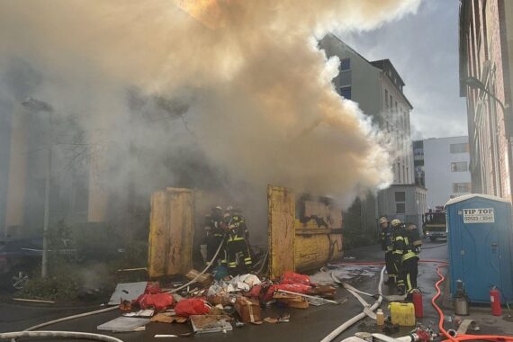 Brand im Müllcontainer, Feuerwehr im Einsatz, Rauchentwicklung, Gefahr für Gebäude, Löschmaßnahmen.