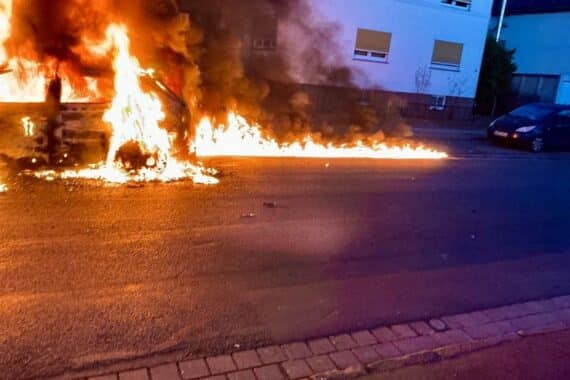 Brennendes Auto, Feuerwehr im Einsatz, Rauchentwicklung, Einsatzkräfte löschen Flammen, Straße gesperrt.
