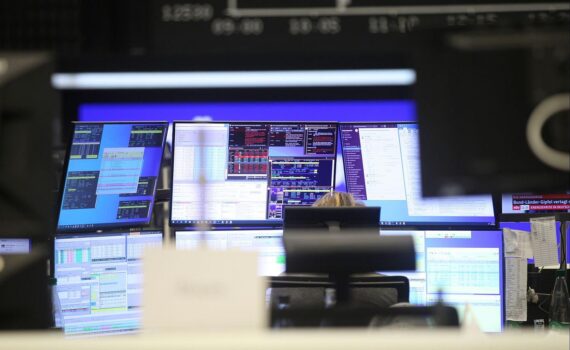 Dax-Chart mit fluktuierenden Kursen, Börsengebäude im Hintergrund und nervösem Handelsumfeld.