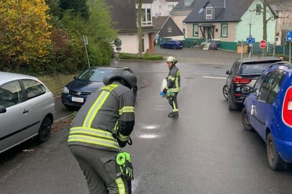 Feuerwehrfrau streut Bindemittel auf einer Ölspur, Warnschilder stehen daneben.