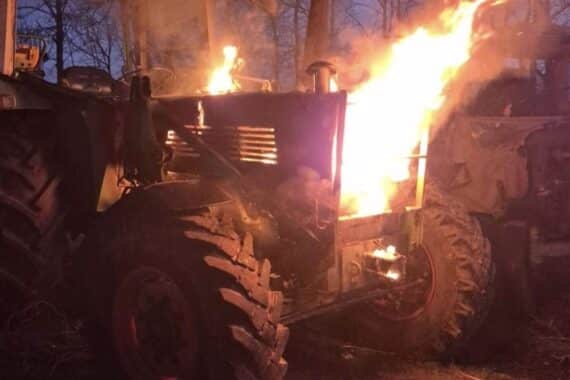 Brennender Traktor gelöscht von Feuerwehr, Einsatzkräfte arbeiten unter Atemschutz, Rauch und Flammen sichtbar.