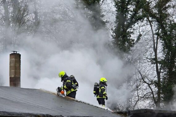 Feuerwehr mit Atemschutz und Säge öffnet Dach, um Brand im Vereinsheim zu lokalisieren.