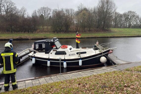 Sportboot im Hafen droht zu versinken, Feuerwehr pumpt Wasser ab, Eigentümer kontrollieren Rumpf.