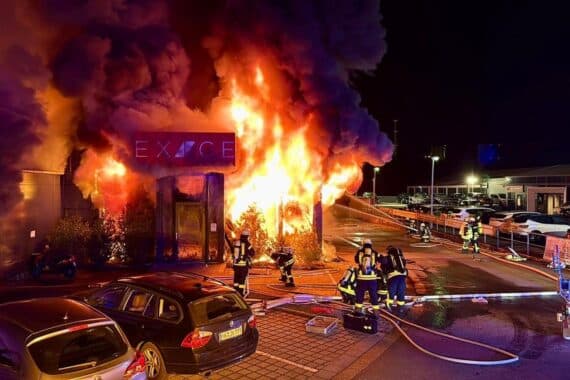 Großbrand in Fitnessstudio: Feuerwehr kämpft gegen Flammen, Personen evakuiert, starkes Feuer sichtbar.