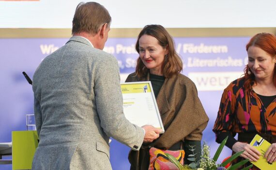 Katerina Poladjan erhält Buchpreis, umringt von Bücherstapeln und feierlicher Atmosphäre.