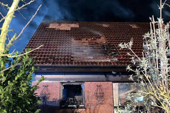 Brand in Wohnhaus, Feuerwehr löscht, beschädigtes Dach, verletzter Bewohner, Einsatzkräfte vor Ort.