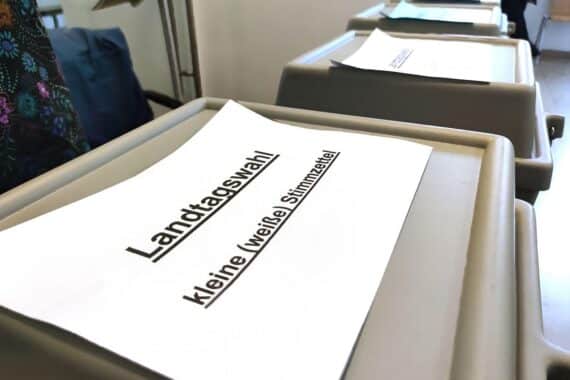 Wahlurne mit Stimmzetteln und Wählern, symbolisch für die Landtagswahl in Rheinland-Pfalz.