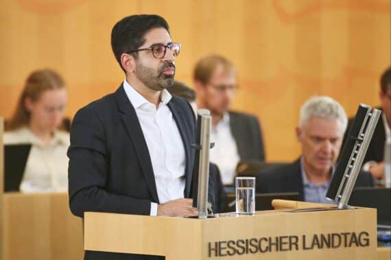 Ein Portrait von Kaweh Mansoori, umgeben von Symbolen für erneuerbare Energien und Tankstellen.