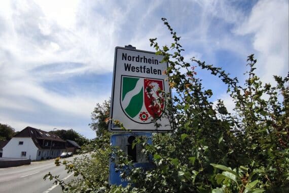 Das Bild zeigt das Landesschild von Nordrhein-Westfalen vor dem Hintergrund einer modernen Stadt.