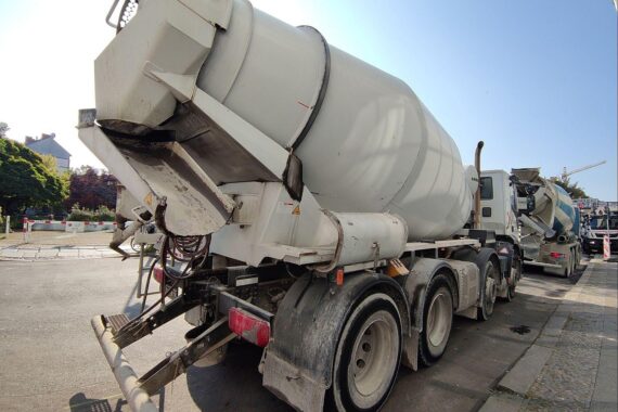 Eine Baustelle mit einem Fahrmischer, Baustellenmaterialien und einem steigenden Energiekosten-Symbol.