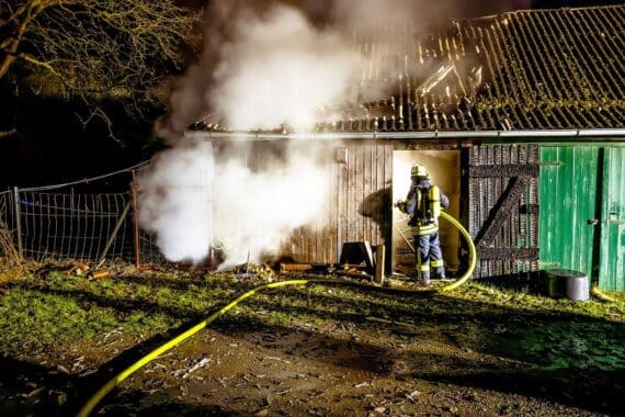 Brennender Schweinestall mit Feuerwehr im Einsatz zur Brandbekämpfung und Schutz der Tiere.