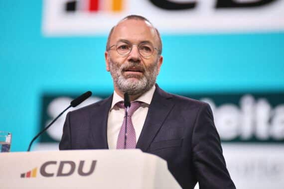 Manfred Weber spricht in Brüssel, umringt von politischen Symbolen und besorgten Gesichtern.