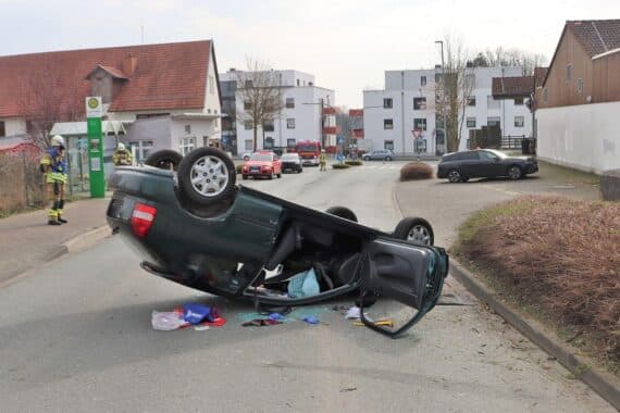 Ein umgekipptes Auto, umgeben von Polizei und Rettungskräften, Unfallstelle auf einer Straße.