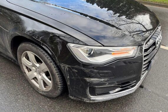 Ein beschädigter schwarzer Audi A6 nach Unfall, mit Polizei-Absperrung und Ermittlern.