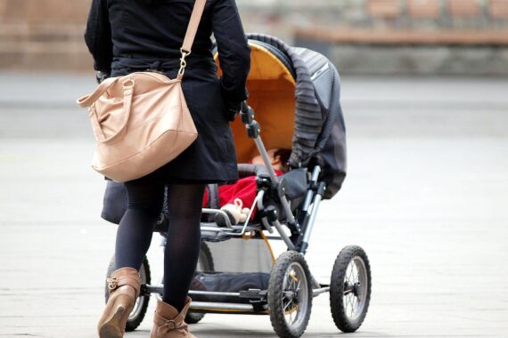 Eine Mutter mit Kleinkind und Kinderwagen symbolisiert die Bedeutung der Hebammenhilfe.