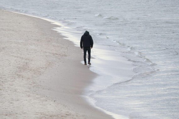 Mann genießt milde Temperaturen am Strand, umgeben von hoher, freundlicher Bewölkung.