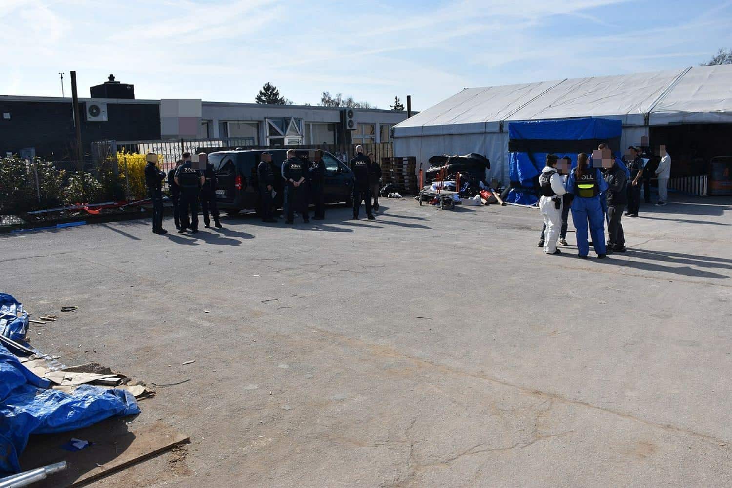 Zollbeamte kontrollieren Arbeiter in Lagerhalle, mutmaßliche illegale Beschäftigung von 15 Chinesen entdeckt.