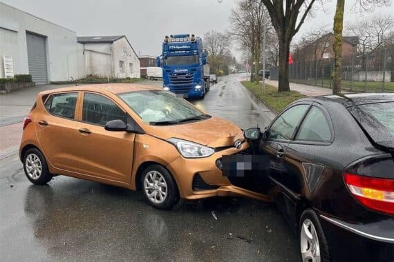 Zwei beschädigte Autos an einer Straße, Rettungswagen und verletzte Personen im Vordergrund.