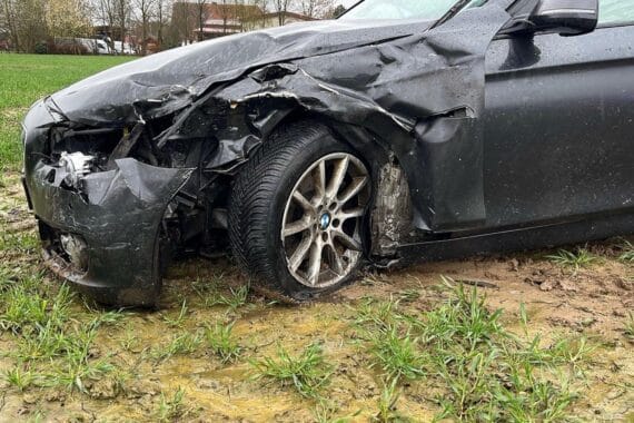 Zwei beschädigte BMW nach Kollision, eins im Feld, Polizei und Rettungswagen vor Ort.