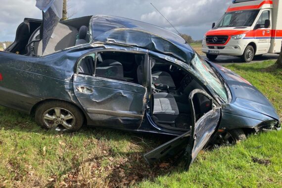 Unfallstelle mit beschädigtem Auto, Bäumen und einer einsamen Straße nach Kollision.