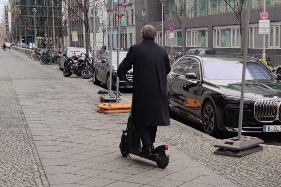Armin Laschet auf E-Scooter, verletzt mit Armstütze nach Unfall, öffentlich unterwegs.