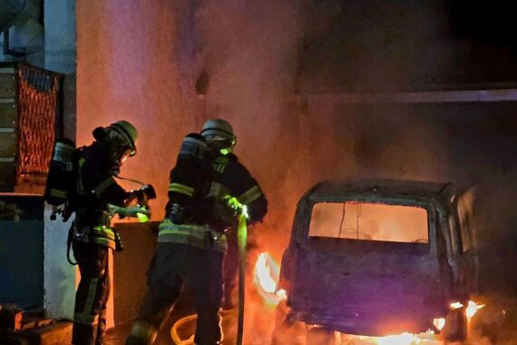 Abgebranntes Auto vor einem Wohnhaus, Feuerwehr im Einsatz, keine Verletzten, Brandursache unklar.